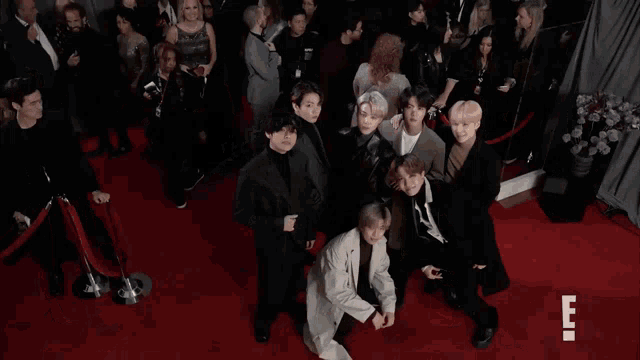 a group of people standing on a red carpet with the letter e on the bottom right
