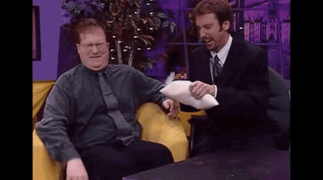 a man in a suit is putting a pillow on another man 's shoulder