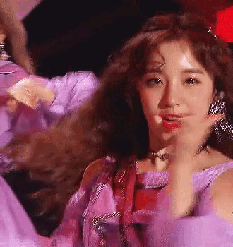 a close up of a woman wearing a purple dress and earrings dancing on a stage .