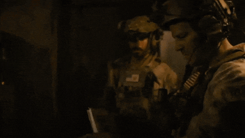 two soldiers are standing in a dark room and one has a patch on his chest that says us army