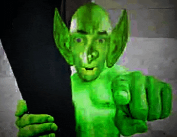 a green monster is pointing at the camera while holding a black object .