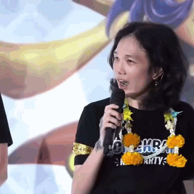 a woman is holding a microphone and wearing a black shirt that says kr