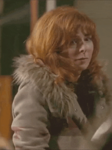 a woman with red hair is wearing a fur hooded jacket and looking at the camera .