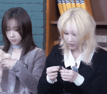 two women are sitting at a table with a book shelf in the background