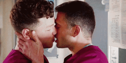 two men are kissing in a room in front of a wall .