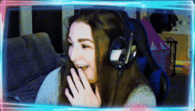 a woman wearing headphones is laughing and covering her mouth with her hand .
