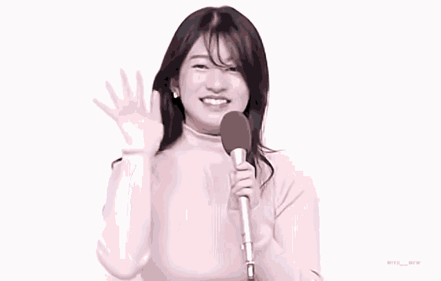 a woman in a pink sweater is waving at the camera while holding a microphone .