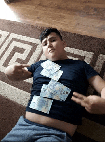 a boy is laying on the floor with money on his stomach and one of the bills says 5