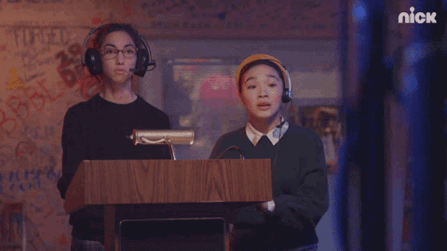 two girls wearing headphones are standing in front of a podium with the nick logo in the corner