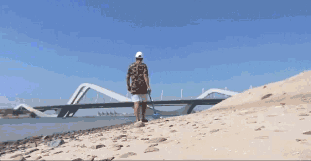 a man walking on a beach with a bridge behind him