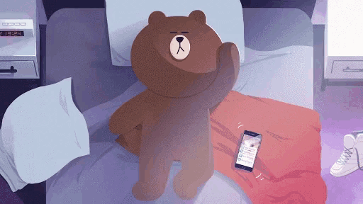 a teddy bear is laying on a bed next to a cellphone