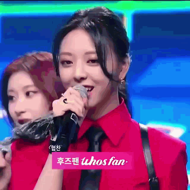a woman in a red shirt and tie is singing into a microphone while another woman watches