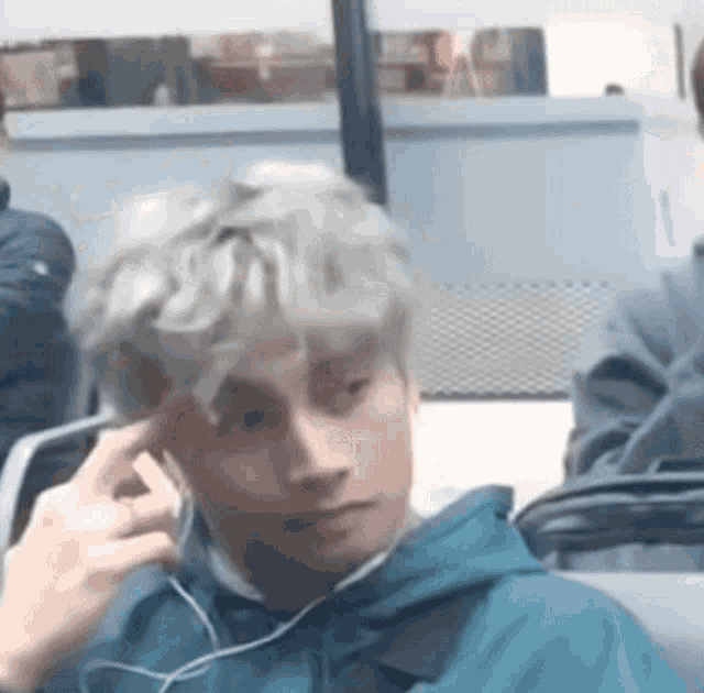 a man wearing headphones and a blue jacket is sitting on a train .
