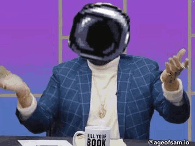 a man wearing a helmet is sitting at a table with a mug that says `` kill your book '' on it .