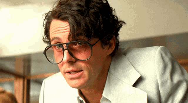 a man wearing glasses and a white jacket looks at the camera