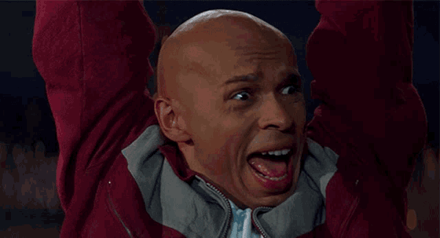 a bald man in a maroon jacket with his mouth open