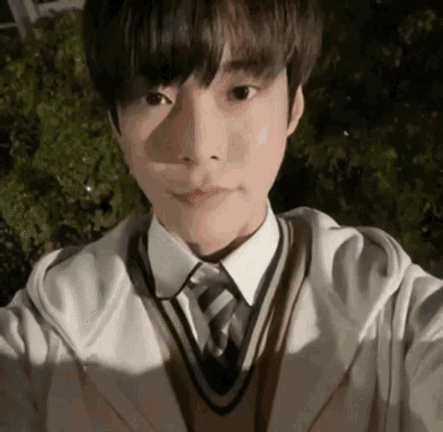 a young man in a school uniform is taking a selfie with his phone .