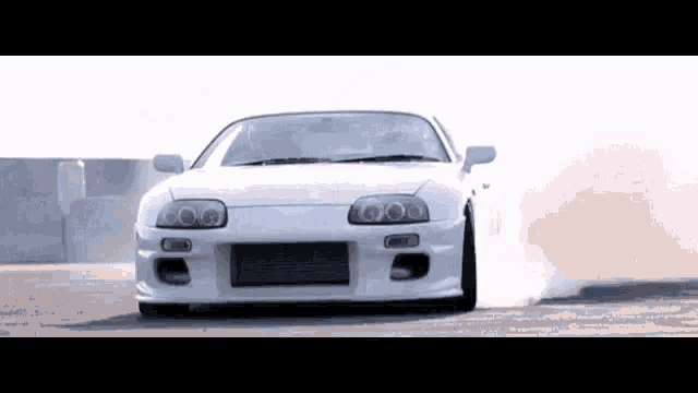 a white sports car is drifting on a road and smoke is coming out of the tires .