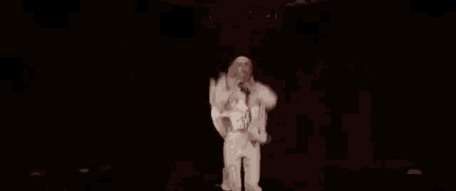 a man in a white suit is standing in front of a microphone in the dark .