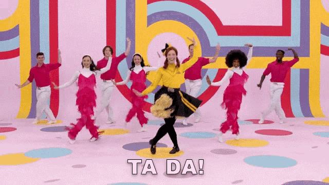 a group of people are dancing in front of a wall with the words ta da written on it