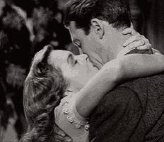 a black and white photo of a man and woman kissing .