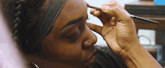 a woman wearing a headband is applying makeup to her eyebrows with a brush .
