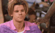 a man in a pink and purple shirt is getting his hair cut .