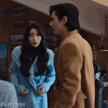 a woman in a blue coat is standing next to a man in a brown suit with divahyunju written on the bottom right