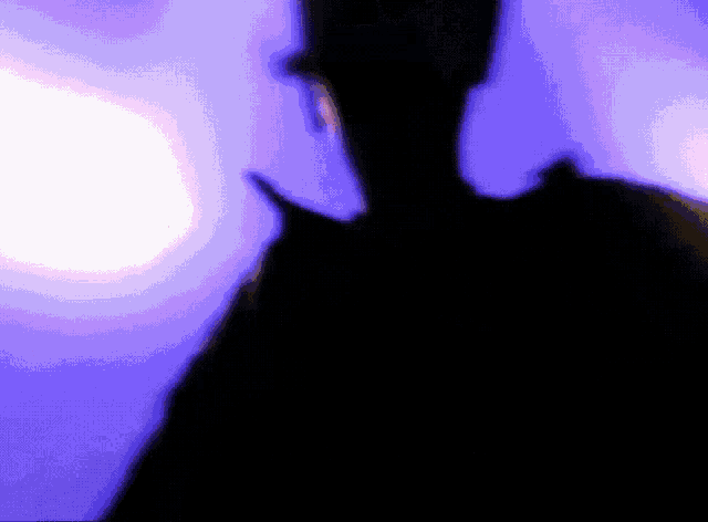 a silhouette of a person standing in front of a purple light