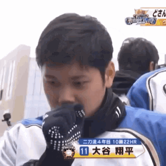 a young man wearing a glove is covering his mouth while standing in front of a group of people .