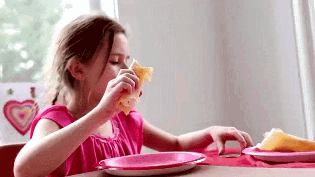 a little girl is sitting at a table eating a sandwich on a plate .