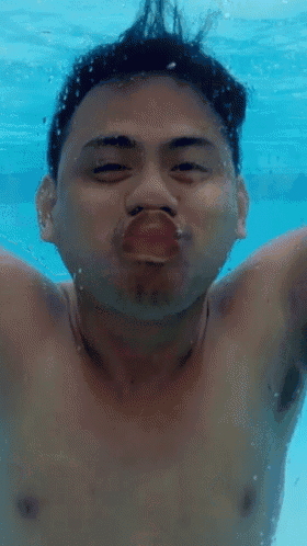 a shirtless man is swimming underwater and making a face