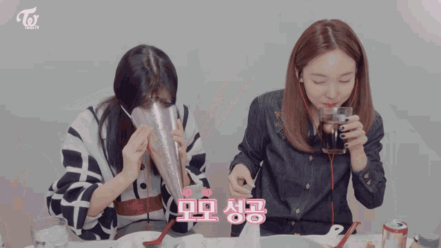 two women sitting at a table with a twice logo on the top left
