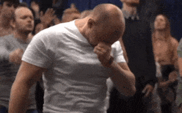 a man in a white shirt is covering his face with his hand while standing in a crowd .