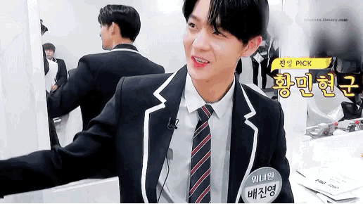 a young man in a suit and tie is standing in front of a mirror and smiling .