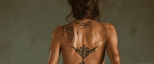 a woman with a tattoo on her back is standing in the rain .
