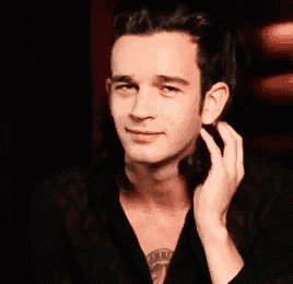 a man with long hair is smiling and touching his face .