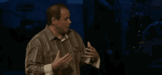 a man in a striped shirt is standing on a stage with a microphone in his mouth .