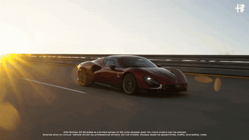 a red alfa romeo car is driving down a highway at sunset
