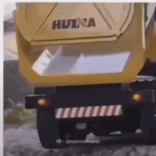 a yellow dump truck is driving down a road with the back door open .