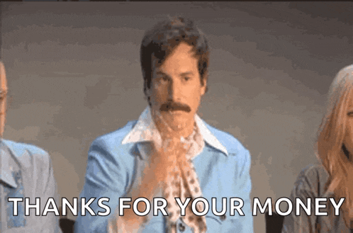 a man with a mustache is sitting in front of a group of people and says thanks for your money