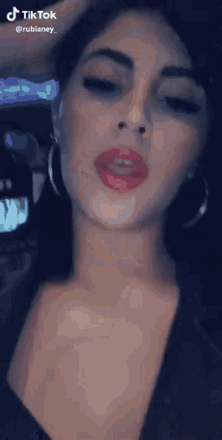 a woman with red lips and hoop earrings is wearing a black top and a black shirt .