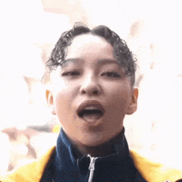 a close up of a woman 's face with her mouth open and a yellow jacket on .