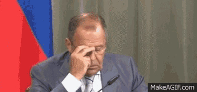 a man in a suit and tie is covering his face with his hand .