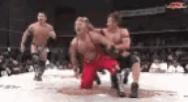 three men are wrestling in a ring and one of them is wearing a red shirt