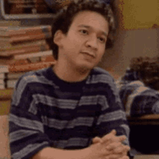 a young man in a striped shirt is sitting at a table with his hands folded .