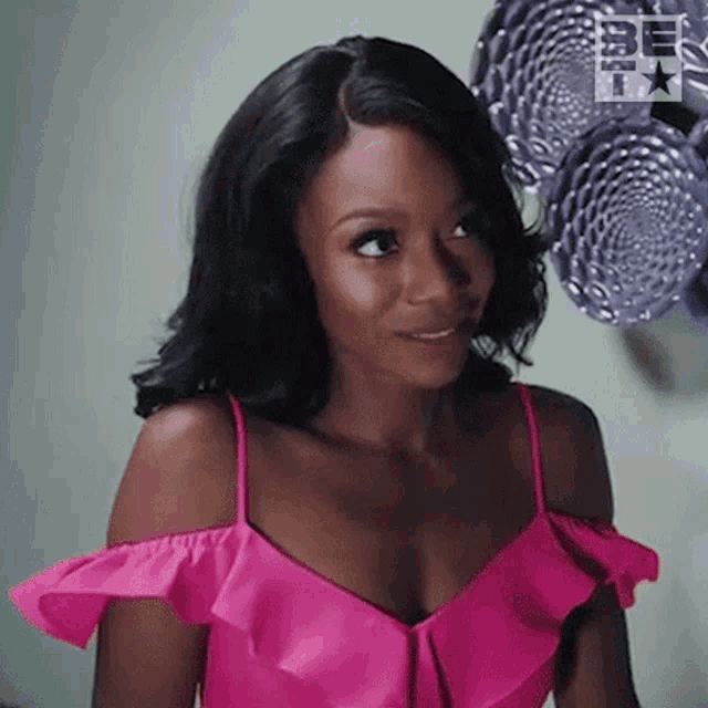 a woman in a pink off the shoulder top is smiling and looking to the side .