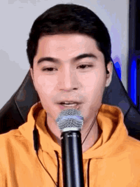 a man in a yellow hoodie is talking into a microphone
