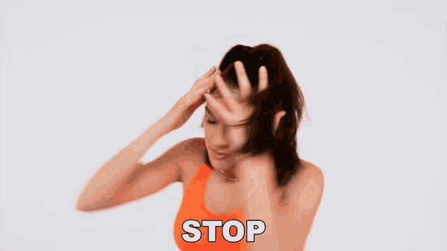 a woman in an orange tank top is holding her hair in front of a stop sign