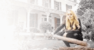 a woman is kneeling down in front of a house holding a large stick .